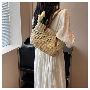 Detail of woven straw shoulder bag with brown leather straps and white floral decor