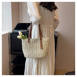 Minimalist cream woven straw beach bag with brown leather handles held by a model