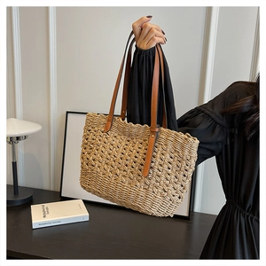 Detail of hand-woven straw tote bag with hollow texture and brown leather handles