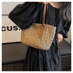 Detailed close-up of beige woven paper straw beach bag with brown leather shoulder straps