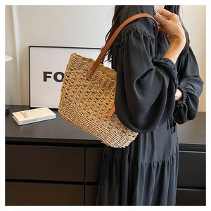 Close-up of woven straw tote bag featuring brown leather shoulder straps and textured fibers