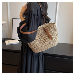 Detail of hand-woven straw tote bag with brown leather handles worn by a female model