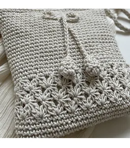 Nahaufnahme der gewebten Blumenstrickstruktur und Zugperle an einer cremefarbenen Tasche