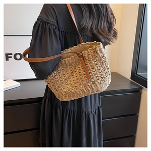 Close-up of woven straw tote bag with brown leather strap and intricate hollow texture