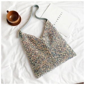 Detail of shimmering sequin tote bag with light blue leather strap on white fabric