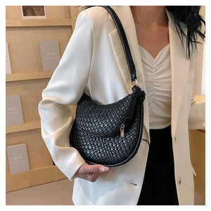 Vue détaillée d'un sac demi-lune tressé noir porté avec un blazer blanc élégant