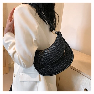 Détail du sac hobo en cuir PU tressé noir avec boucle en métal doré sur un costume blanc