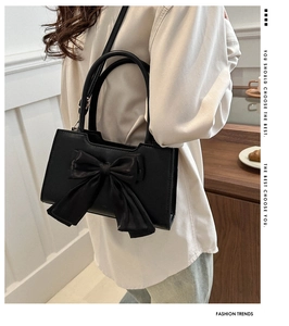 Sac à main en cuir mat noir avec grand nœud élégant porté par un mannequin en intérieur