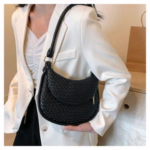 Détail du sac à main noir tressé en cuir PU avec boucle dorée sur un blazer blanc