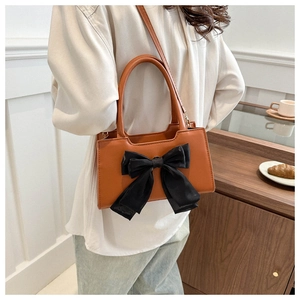 Sac bandoulière en similicuir marron avec grand nœud en mousseline noire dans un café