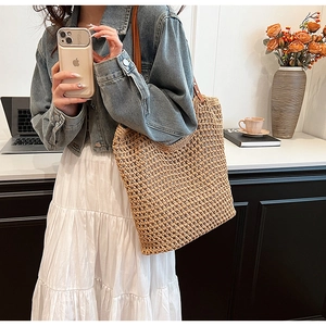Close-up of intricate hollow straw weave texture and brown leather strap on a tote bag
