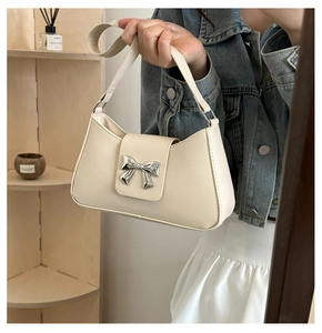 Close-up of a cream PU leather shoulder bag featuring a silver metal bow buckle detail
