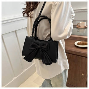 Détail du sac à bandoulière noir en PU avec grand nœud en satin dans un décor de café chic