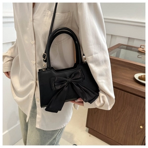 Détail d'un sac cabas en cuir noir avec un grand nœud dans un décor de café chaleureux