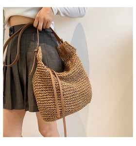 Detail of hand-woven straw tote bag with brown leather shoulder strap and natural texture