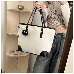 Detail of minimalist beige tote bag with black trim and plush charm in home setting