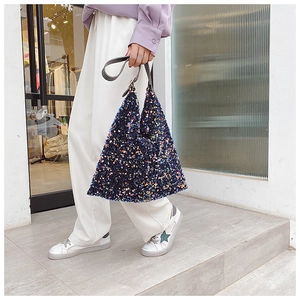 Close-up of colorful sequins on a navy tote bag with grey leather straps and handle