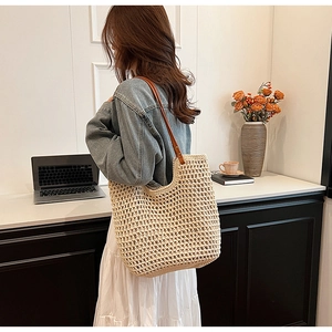 Detail of a beige woven straw tote bag with brown leather shoulder straps shown on a shoulder