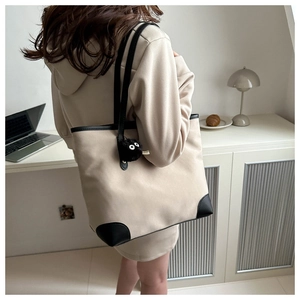 Detail view of stylish beige tote bag with black trim and cute plush ball charm on shoulder