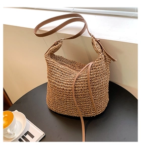 Detail of hand-woven straw shoulder bag with brown leather strap on a black table