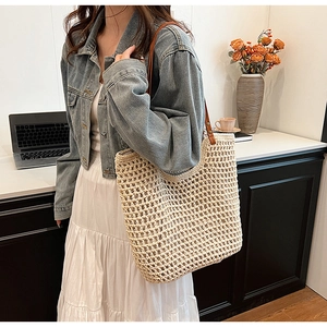 Detailed view of beige hollow woven tote bag with brown leather handles on a model