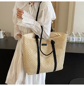 Close-up of beige straw tote bag with black rope handles and contrast leather patch
