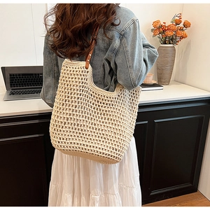 Detail of beige straw woven tote bag featuring brown leather straps and mesh design