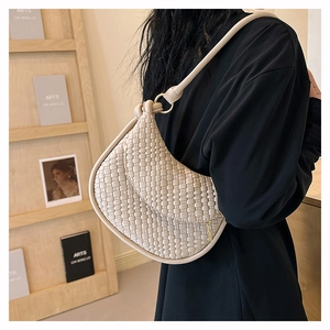 Gros plan du sac hobo tressé crème à l'épaule, montrant la texture minimaliste raffinée
