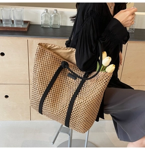 Detail of hand-woven straw tote bag with black rope handles in a modern home setting