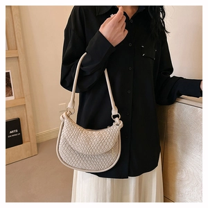 Détail de la texture tressée beige et de l'anneau métallique sur le sac hobo demi-lune