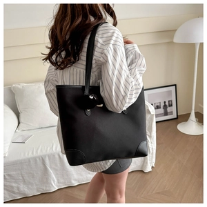 Detail of black tote bag with reinforced leather corners and coal ball charm in home setting