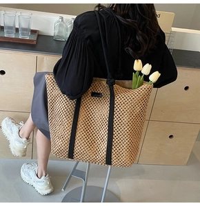 Close-up of woven straw tote bag featuring black straps and diamond knit texture