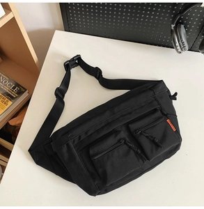 Détail du sac bandoulière en nylon noir avec poches zippées et étiquette de marque orange