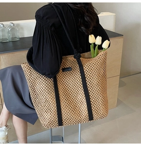 Detail of hand-woven straw tote bag with black canvas straps and minimalist tag