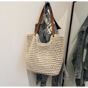 Fashionable woven straw tote bag with brown leather straps hanging on a wall hook