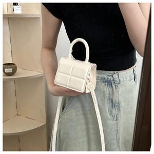Detailed macro view of white quilted mini handbag with top handle and golden hardware