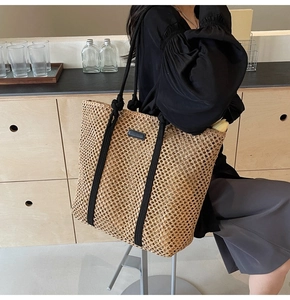 Detail of hand-woven straw tote bag with black rope handles and minimalist leather patch