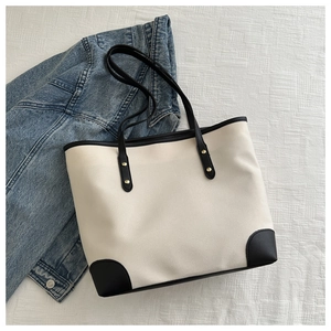 Minimalist canvas tote bag with black leather trim and handles shown on a denim background