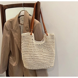 Handmade woven straw tote bag with brown leather shoulder straps on a wood frame