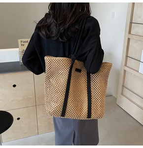 Detail of a large straw woven tote bag with black straps and mesh design on a model