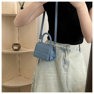 Detail of light blue padded PU leather handbag featuring square quilting and a round handle