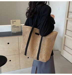 Detail of hand-woven straw tote bag with black canvas straps on a female shoulder