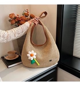 Detail of hand-woven straw hobo bag with brown leather trim and white daisy charm