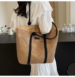 Large woven straw tote bag with black handles on shoulder in cafe setting