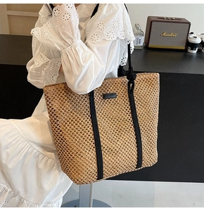 Close-up of a large capacity straw tote bag with black rope handles and leather patches