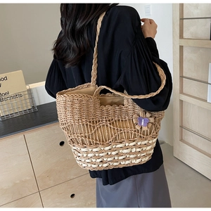 Détail d'un sac cabas en paille tissée avec rayures blanches et charm papillon violet