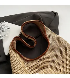 Detail of woven straw tote bag with brown leather shoulder strap on grey suit fabric