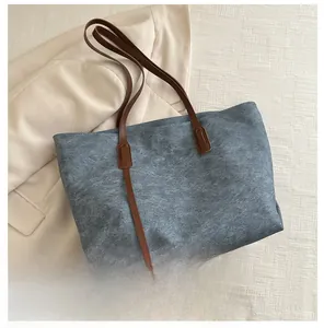 Borsa tote in denim blu con manici marroni mostrata accanto a uno smartphone per le dimensioni
