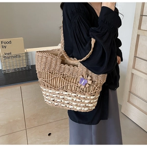 Détail du sac cabas en paille tissée avec motifs ajourés et breloque fleur mauve