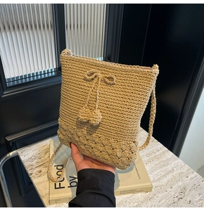 Detailansicht der handgefertigten Strohtasche mit Lochmustern und Bommelanhängern